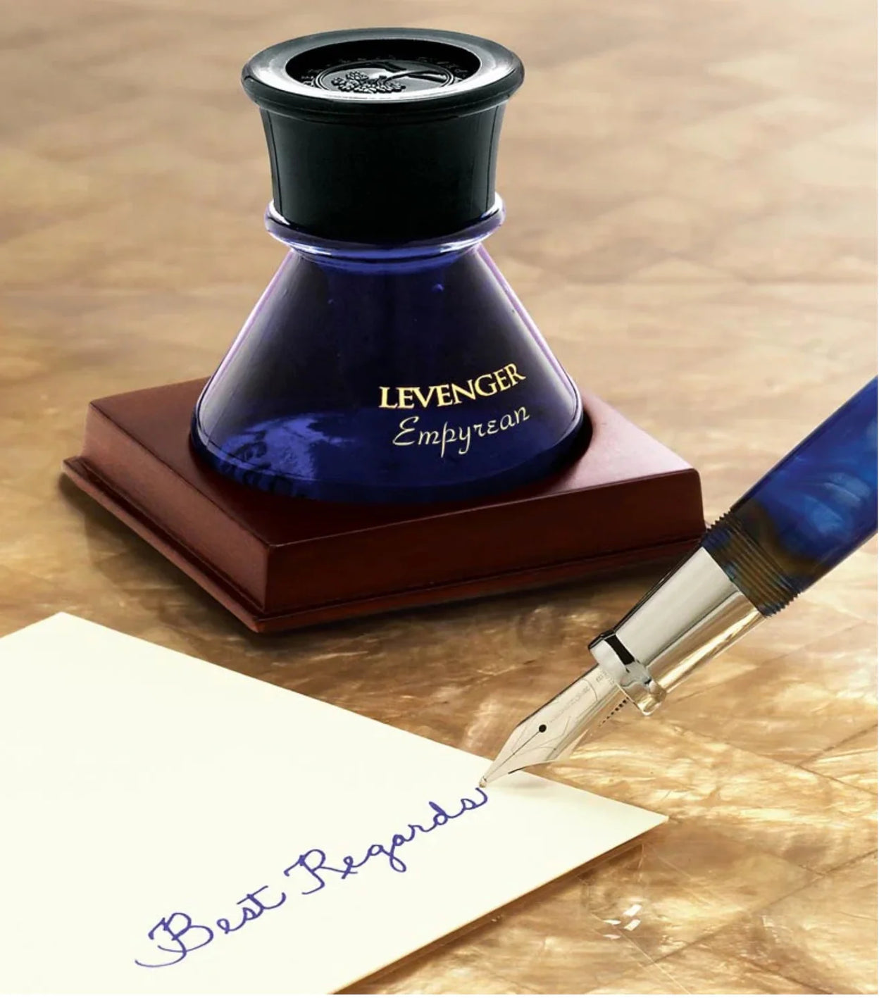 A Levenger fountain pen beside bottled ink and a selection of ballpoint and rollerball refills arranged on a writing desk.