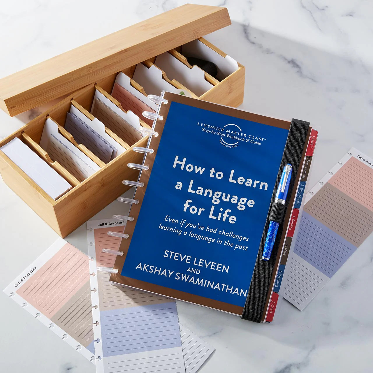 A Levenger Circa smartPlanner open to a weekly layout beside a classic bound planner on a wood desk, with discs, refill sheets, and a fountain pen in view.