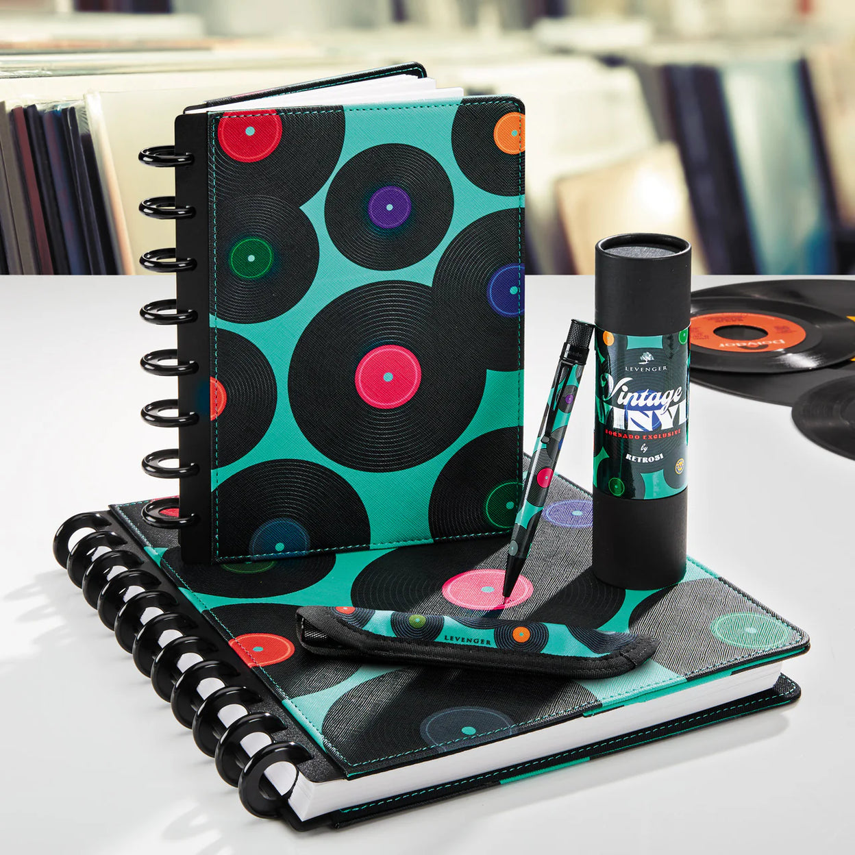 A Levenger Circa notebook with a subtle leather monogram, translucent cover with printed initials, and contrasting aluminum discs laid out with color-coordinated accessories.