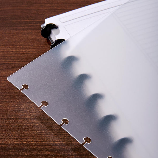 Translucent discbound notebook cover with punched holes and rings on a wooden desk